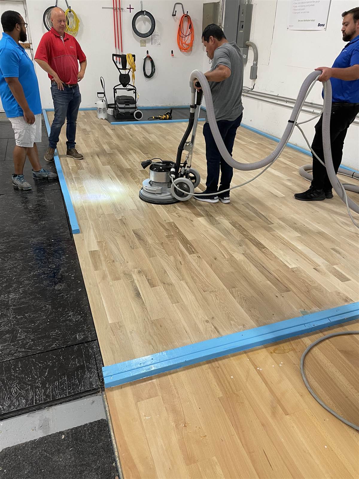 Students and instructor operating a Bona floor sander and dust collection hose on a freshly sanded hardwood floor during certification training