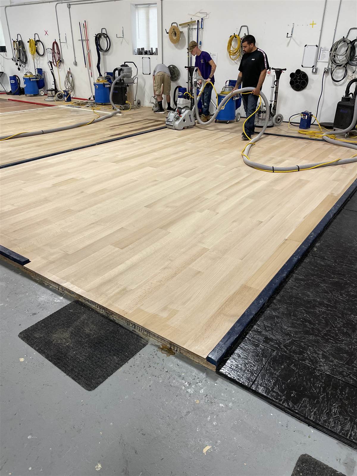 Row of professional Bona floor sanding equipment lined up beside a freshly refinished hardwood training floor